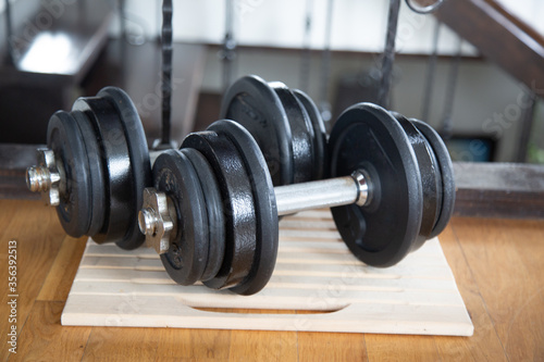 Two Black gym dumbbells with disks on the wooden floor indoor. Sport at home