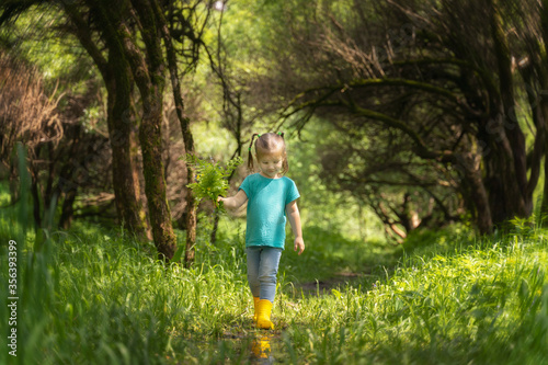 Little girl walks through puddles in rubber boots in the woods