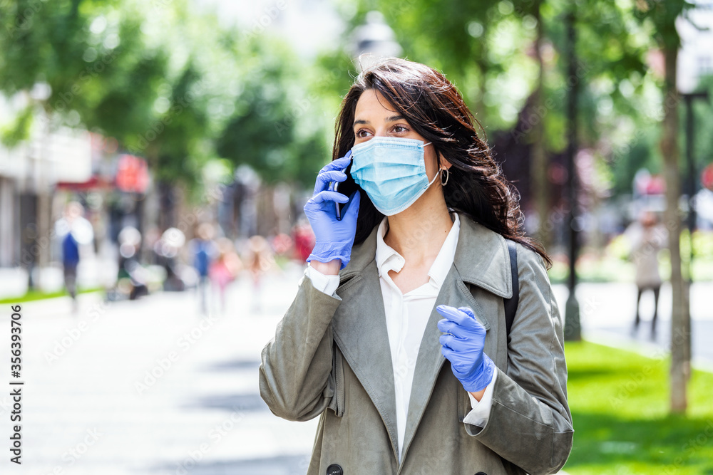 Portrait of young woman on the street wearing face protective mask to prevent Coronavirus and anti-smog and using smartphone