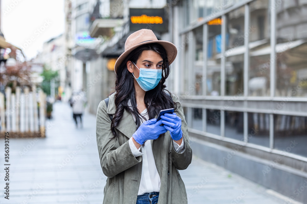 Fototapeta premium Portrait of a young woman wile wearing a face mask for protection from cold and flu and viruses. Young woman with face mask in the street. Woman wearing face mask because of air pollution in the city
