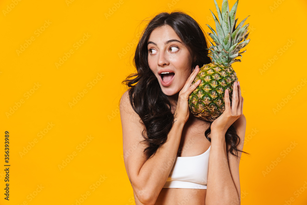 Image of excited brunette woman holding pineapple and looking aside Image of excited brunette woman holding pineapple and looking aside