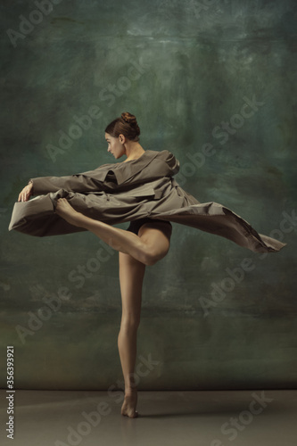 Warm. Graceful classic ballerina dancing, posing isolated on dark studio background. Stylish trench coat. Grace, movement, action and motion concept. Looks weightless, flexible. Fashionable, style.