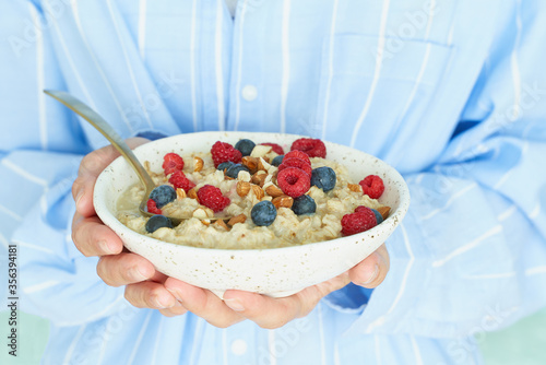 Faceless woman holds in hands breakfast, oatmeal porridge with berries and nuts photo