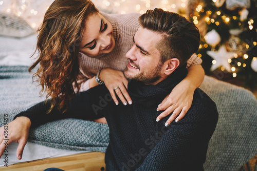 Young family dressed in knitwear looking at camera celebrating Christmas together at cozy apartments