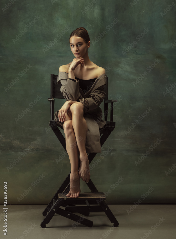 Beautiful portrait. Graceful classic ballerina dancing, posing isolated on dark studio background. Stylish trench coat. Grace, movement, action and motion concept. Looks weightless, flexible.