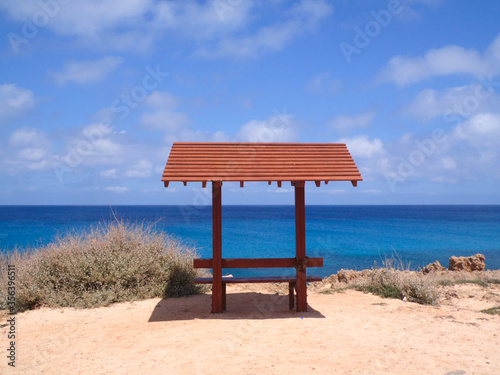 Beutiful lonely wooden sitting bench in front of the sea, blue sky with clouds