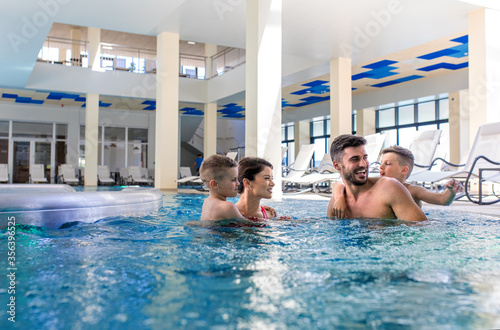 Smiling family of four having fun and relaxing in indoor swimming pool at hotel resort. © Zoran Zeremski