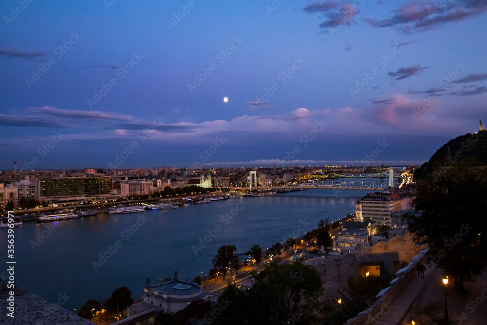 Night aerial panorama of Budapest with Elisabeth Bridge and river boats and moon on Danube river illuminated with night lights.