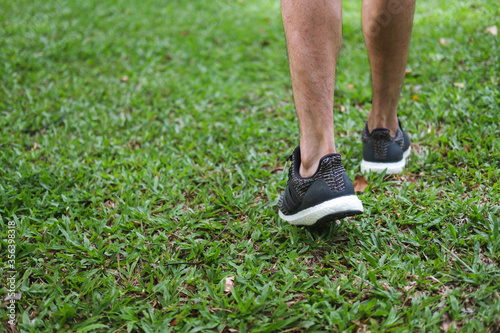 man wearing black sneaker shoe walk in grass park. close up view into foot and leg.
