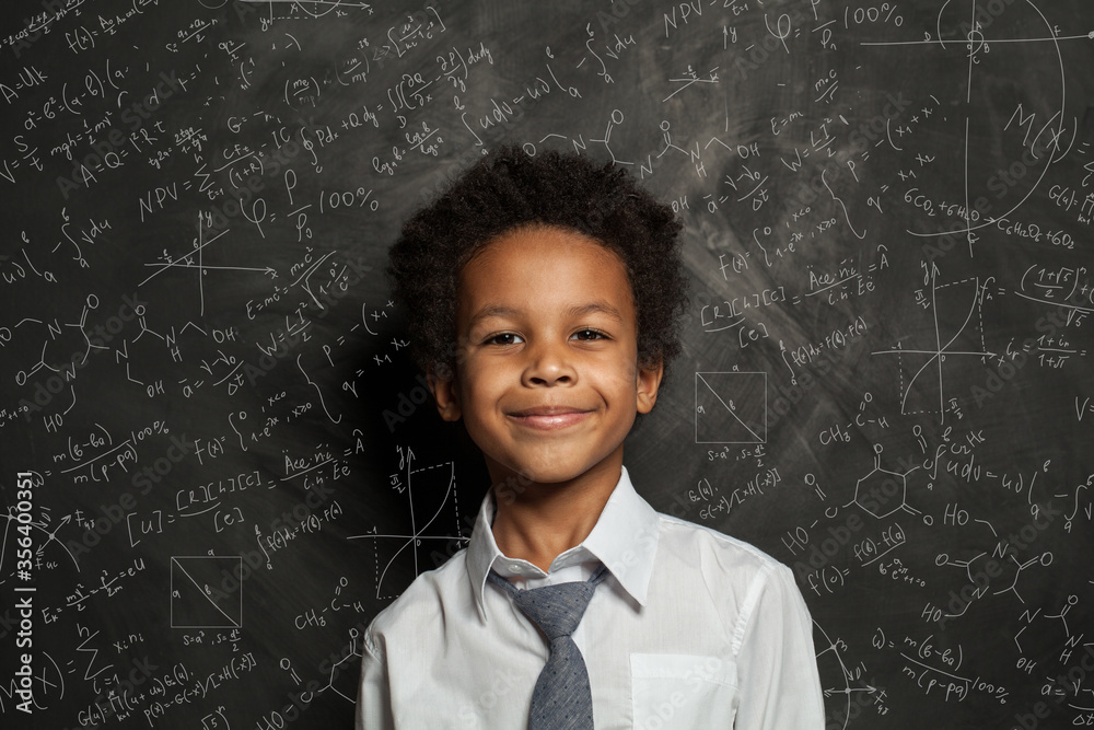 Happy smart black child student on blackboard background with science and maths formulas Happy smart black child student on blackboard background with science and maths formulas
