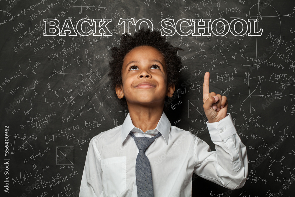 Clever black kid boy student pointing at chalkboard with back to school inscription Clever black kid boy student pointing at chalkboard with back to school inscription