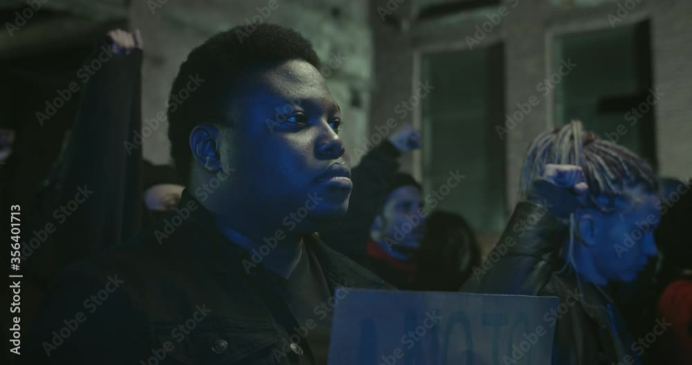 Crop view of afro american man holding placard while standing in crowd of protesters at night street. Strike against police brutality, racism and fatal use of force by officers