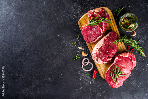 Raw meat, beef steak on cutting board with rosemary and spices, black background, top view copy space
