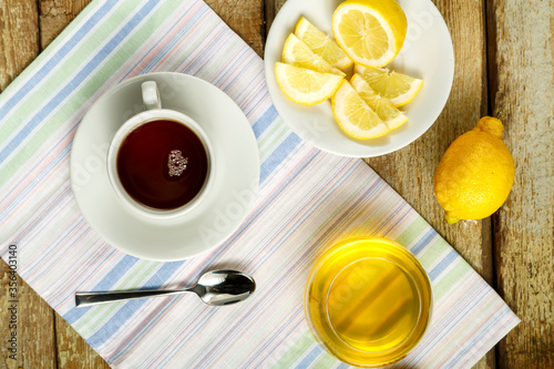 White cup with tea with lemon and honey on a table on a napkin.