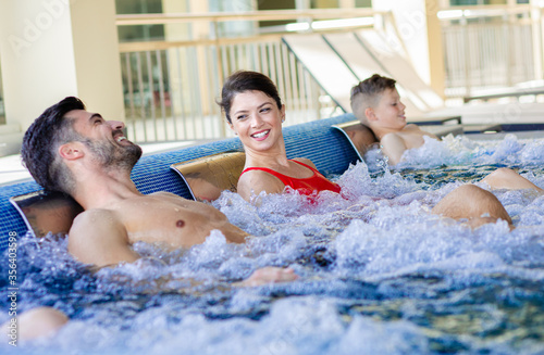 Smiling family of three having fun and relaxing in indoor swimming pool at hotel resort.