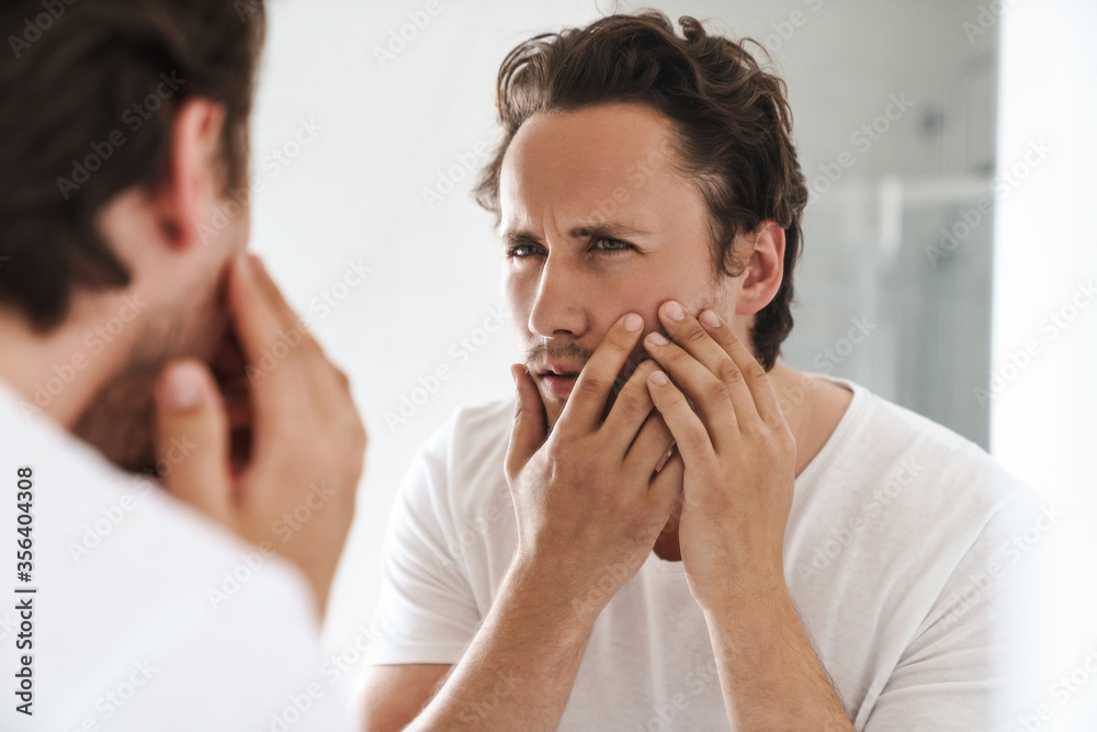 Attractive young man standing in front of the bathroom mirror Attractive young man standing in front of the bathroom mirror