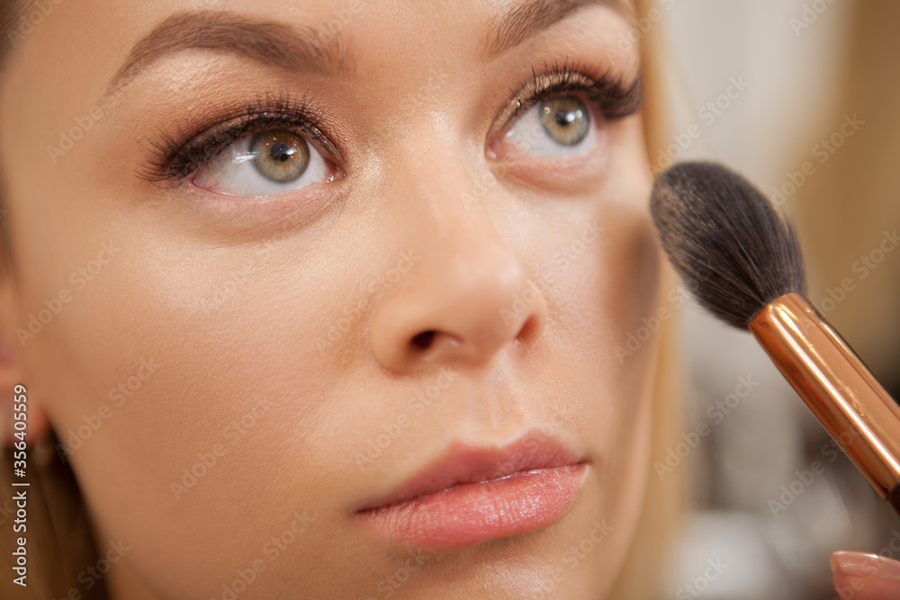 Cropped close up of a professional makeup artist applying highlighter on the face of beautiful woman Cropped close up of a professional makeup artist applying highlighter on the face of beautiful woman