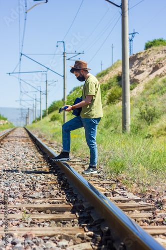 man with protective mask on railroad tracks playing on guitar
