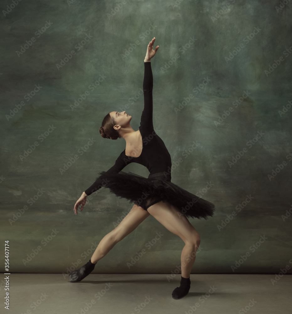 Dancing night. Graceful classic ballerina dancing, posing isolated on dark studio background. Elegance black tutu. Grace, movement, action and motion concept. Looks weightless, flexible. Fashionable.