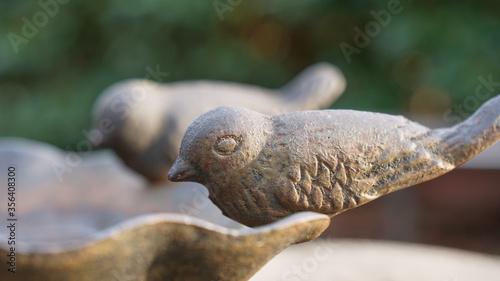 Side view of two small decorative metal birds sitting on the edge of a clam shaped bird bath in the late autumn sun