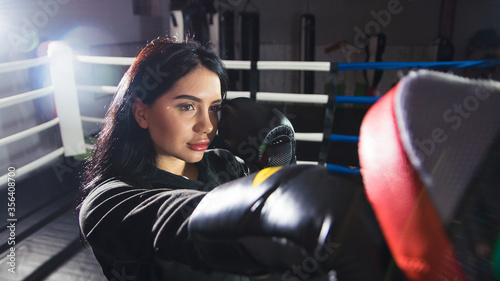 A beautiful girl in boxing gloves hits her paws in the ring. Sexy woman is training in the gym. Beautiful brunette is engaged in boxing. web banner