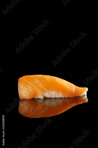 Japanese Cuisine - Appetizing Salmon Sushi Set, Nigiri. Philadelphia Sushi Roll - Maki Sushi with Philadelphia Cheese inside on mirror black background. Smoked salmon rolls served on a plate