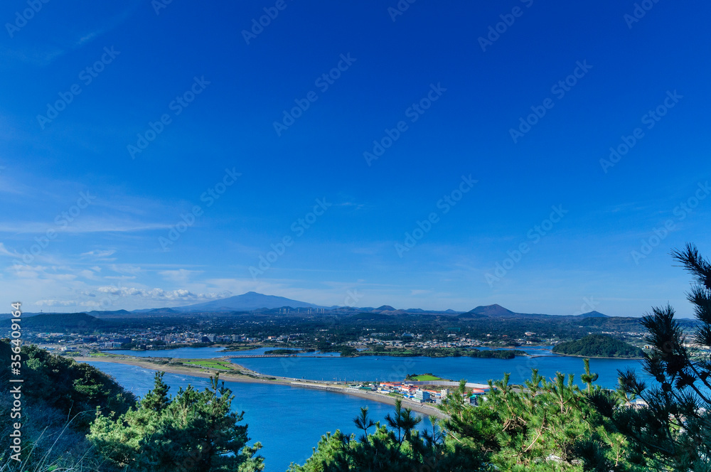 awesome view of seaside small city within seongsun ilchubong jeju island south korea with yellowish grass foreground and slightly cloudy blue sky and ocean. Visible at far is mountain area`