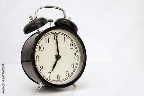 Black vintage alarm clock on table. White background. Wake up concept. An image of a retro clock showing 07:00 pm/am. 