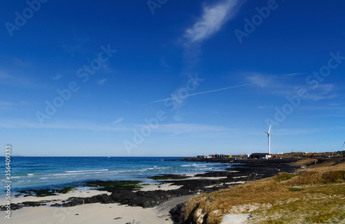 Beautiful view Woljeong Beach with leading line to white windmill at far right at Jeju Island South Korea backed by awesome blue sky background.