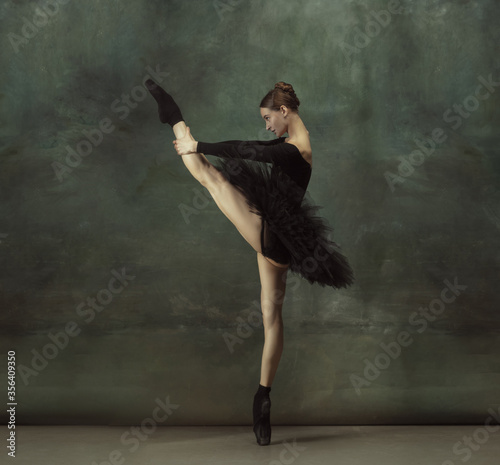 Dancing night. Graceful classic ballerina dancing, posing isolated on dark studio background. Elegance black tutu. Grace, movement, action and motion concept. Looks weightless, flexible. Fashionable.