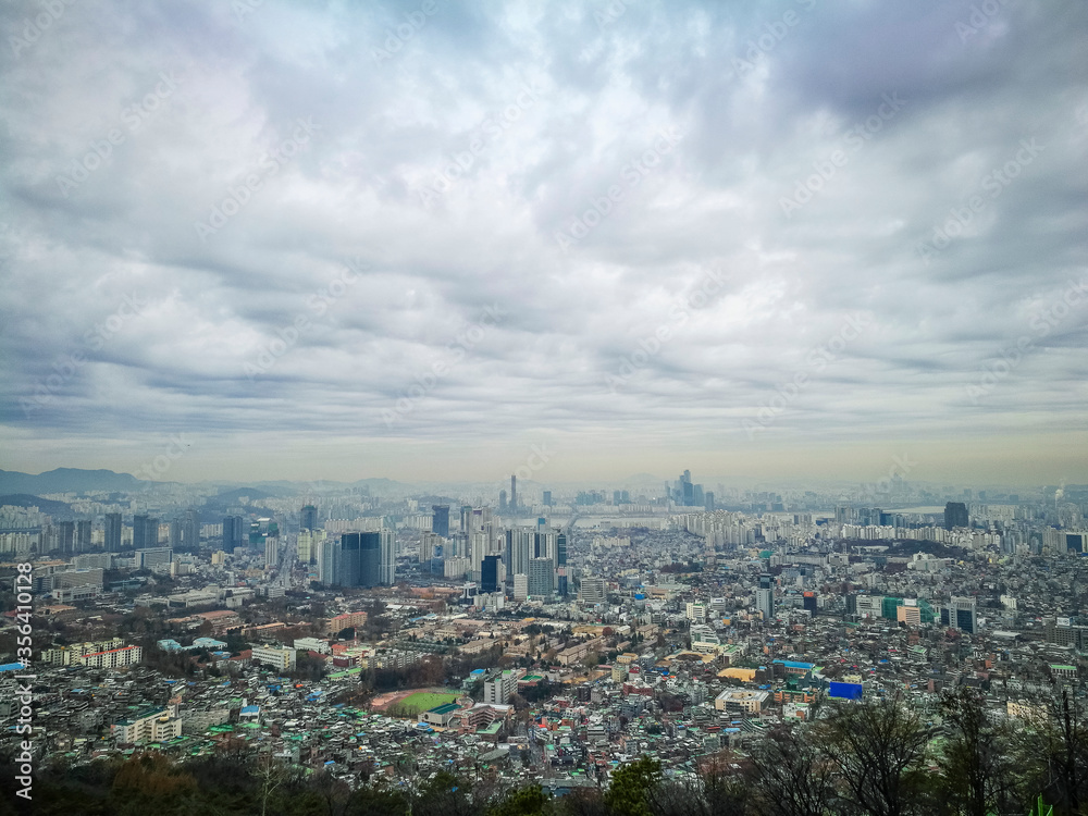 High angle view of part of capital city of Seoul from high ground at namsan Seoul South Korea. Visible noise and soft focus due to foggy and cloudy morning. Cloudy blue sky at background.