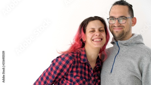 Man and woman looking at the camera and smiling woman explains a thought to a man and shows her open palm towards the camera. Modern hipster family. Wife with pink hair and husband with ponytail