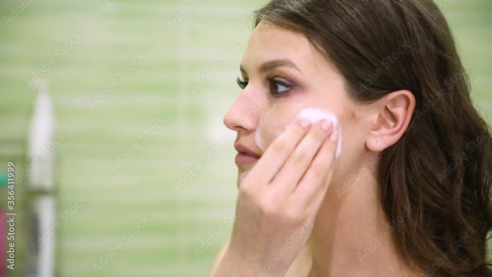 girl removes makeup using a cotton pad in a green bathroom girl removes makeup using a cotton pad in a green bathroom