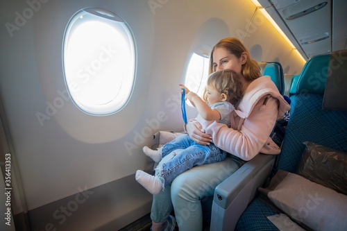concept - comfortable flight with a child. young beautiful mother is sitting in an airplane chair holding on her lap a little cute toddler. kid plays