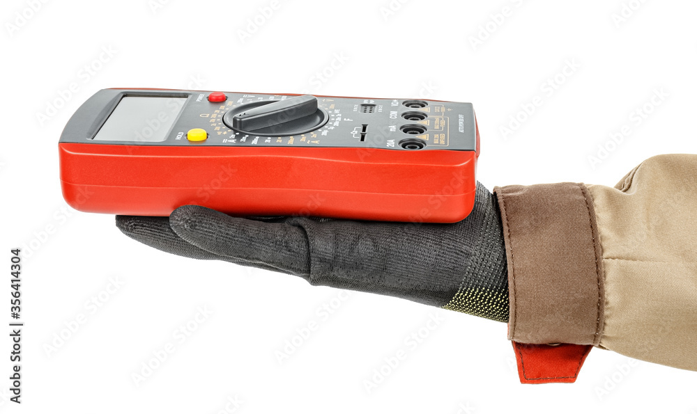 Digital multimeter with red rubber protective case lies on palm of electrician hand in black protective glove and brown uniform isolated on white background