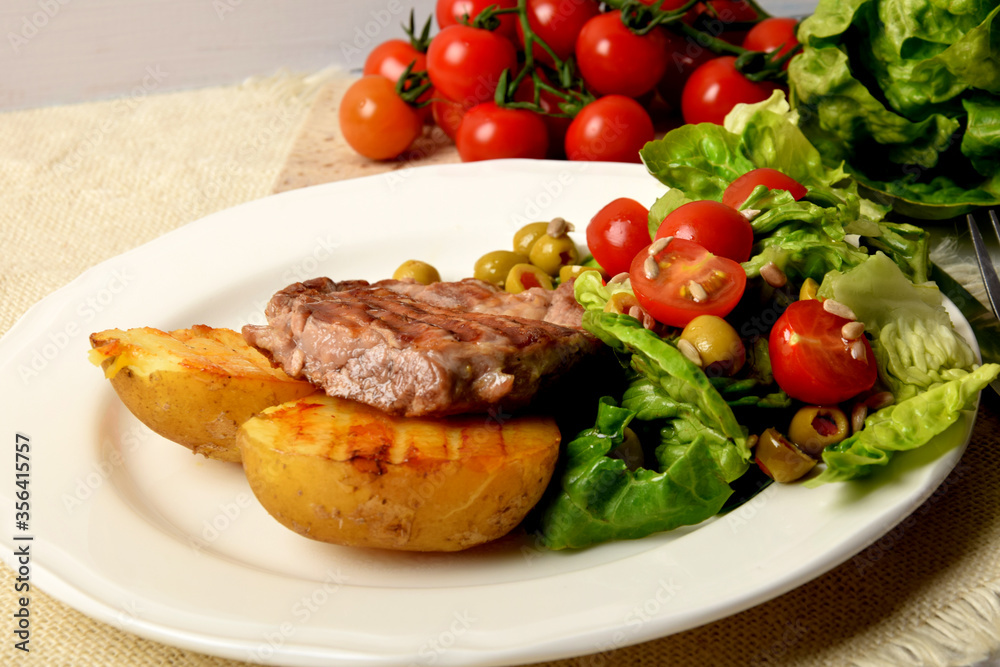 two pieces of grilled potato and grilled meat next to lettuce with tomatoes and olives on a white plate two pieces of grilled potato and grilled meat next to lettuce with tomatoes and olives on a white plate