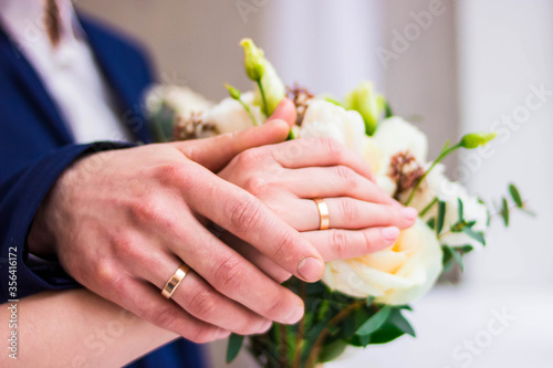 Hands with gold rings, accessories on the wedding day, bride's bouquet in the background, newlyweds