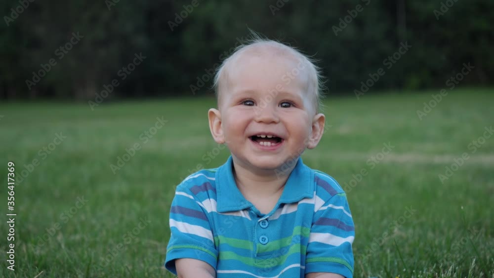 Portrait Of A Funny Cute Blond Kid Sitting On The Lawn And Smiling Portrait Of A Funny Cute Blond Kid Sitting On The Lawn And Smiling