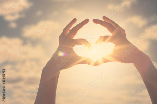 Hand heart shape silhouette made against the sun and sky of a sunrise or sunset.