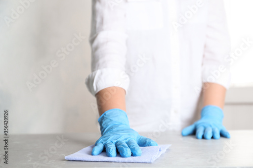 Woman in gloves wiping grey marble table with rag indoors, closeup