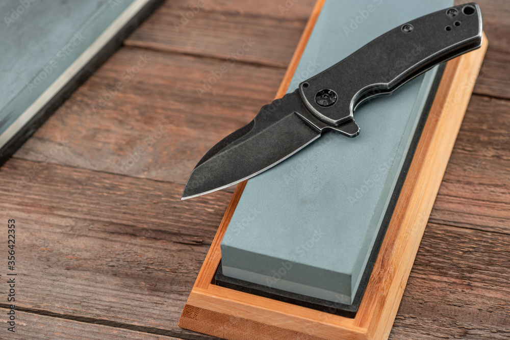 Steel pocket knife and whetstone on a rustic wooden background Steel pocket knife and whetstone on a rustic wooden background