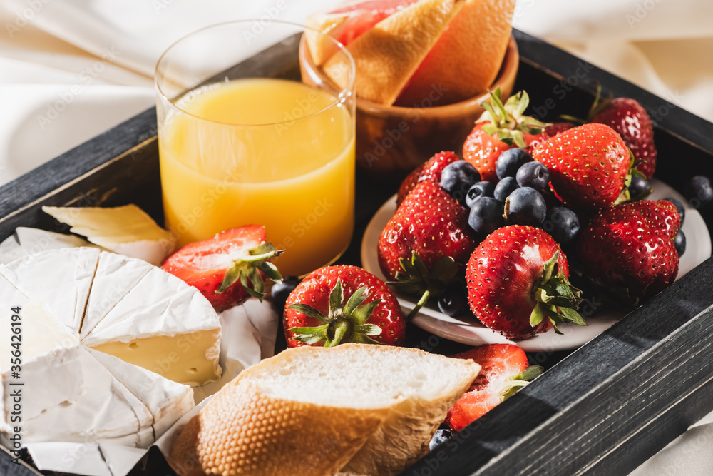 close up view of french breakfast with grapefruit, Camembert, orange juice, berries and baguette on wooden tray