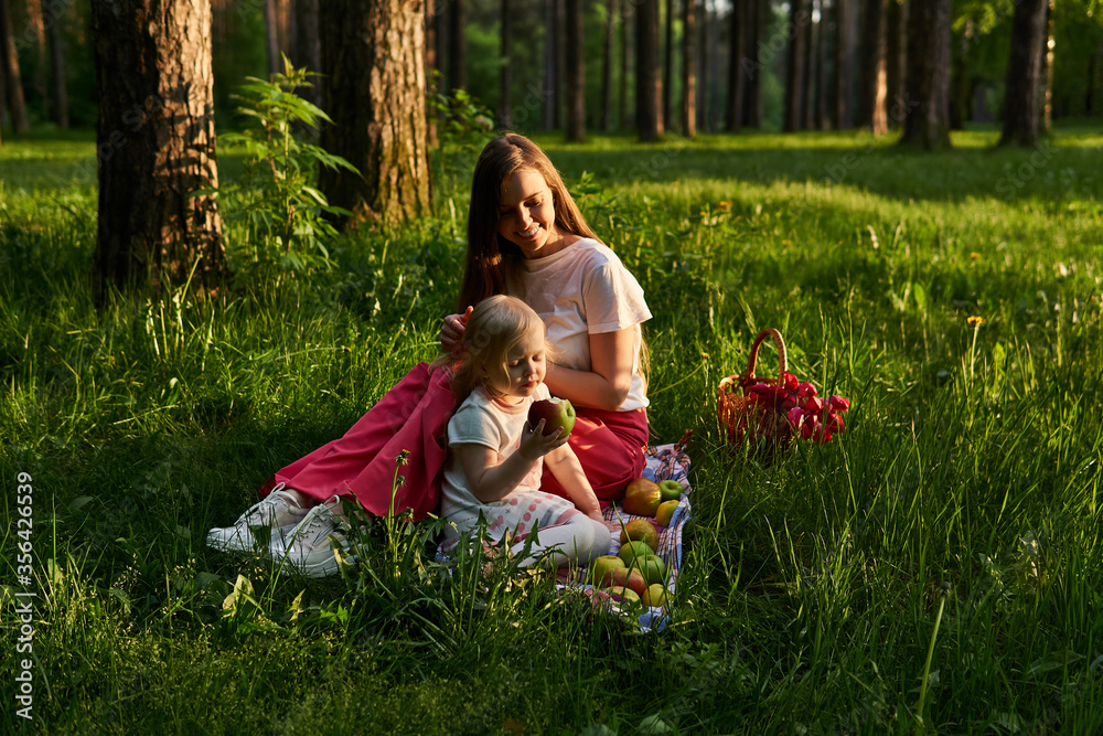 Fototapeta premium little girl eats an apple in nature during a picnic with her mom