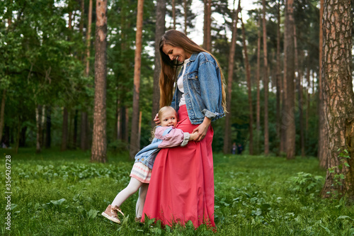 happy child girl hugs her mom standing on the grass in the park
