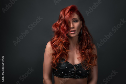 sexy girl posing against black background with copy space. beautiful woman wearing leather top bra with sparkling stars. red colored hair and professional make up © Alexander