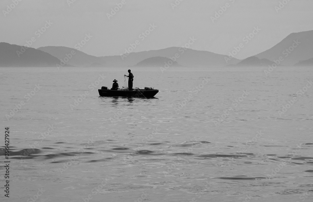 Silhouette of fisherman on a boat in the ocean with mountains in the background