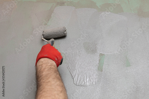 A close-up view of an experienced construction worker applying damp insulation using a paint roller on a wall. photo