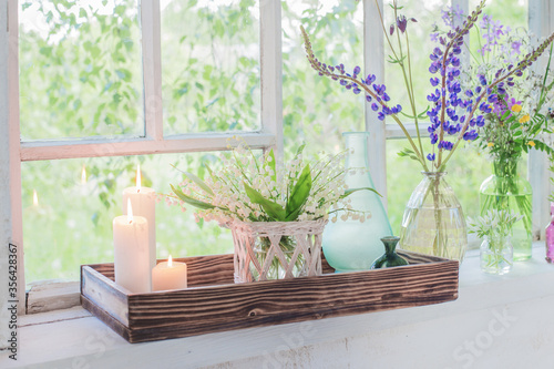 flowers with burning candles on white windowsill