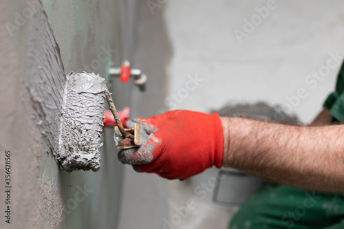 A close-up view of an experienced construction worker applying damp insulation using a paint roller on a wall. photo