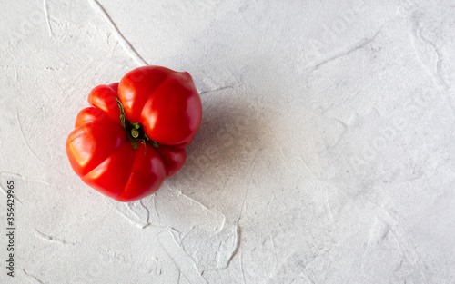 Unshaped red tomato on grey concrete background. Top view, copy space photo